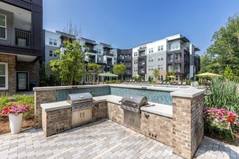 An outdoor kitchen with two grills next to a pool with an apartment building in the background